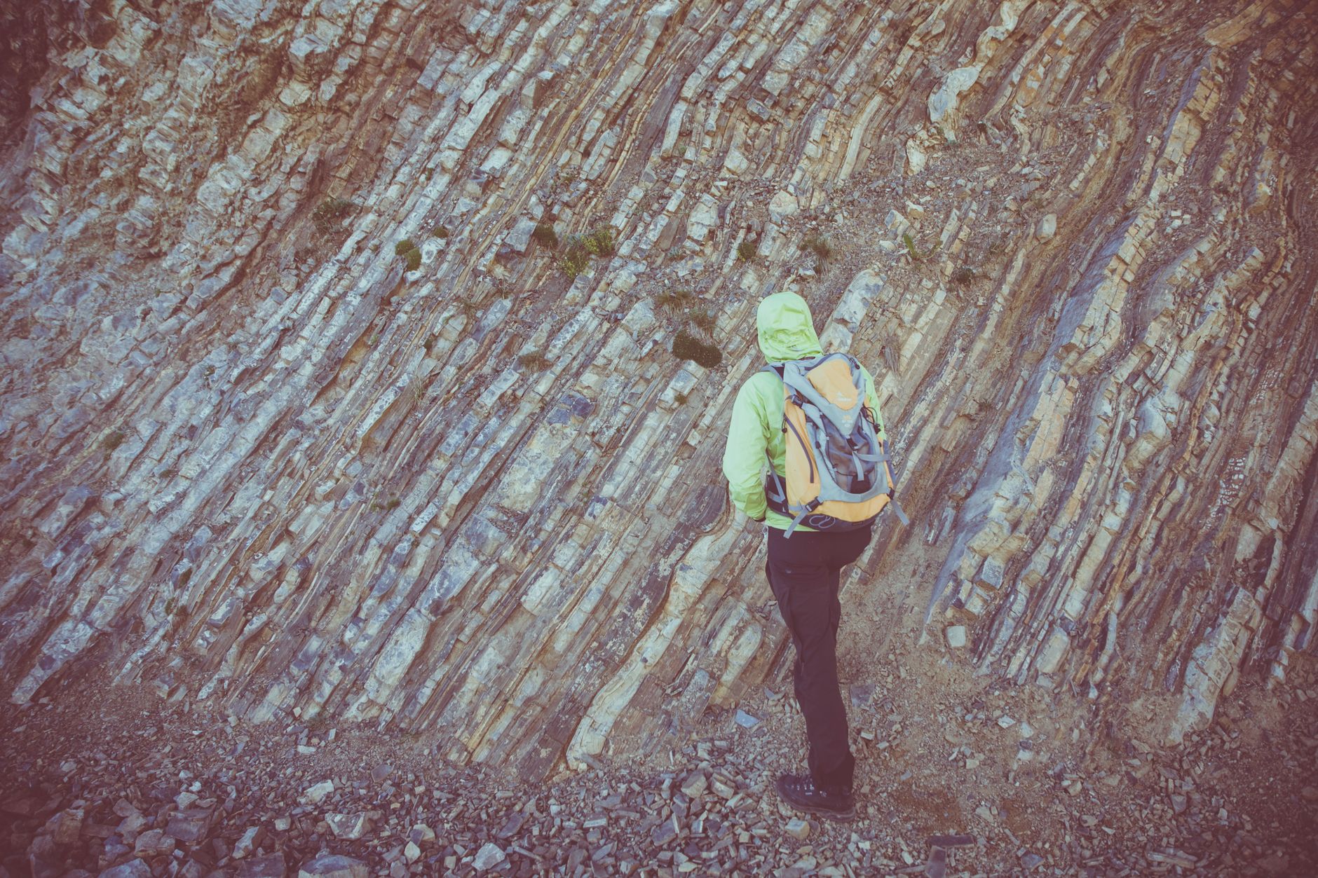 A lone hiker with a backpack explores the rugged and textured rocky mountain surface.