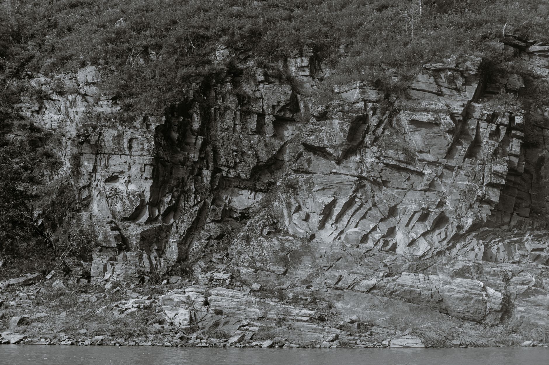 Black and white of dry mount with bumpy surface and growing grass against river in daytime