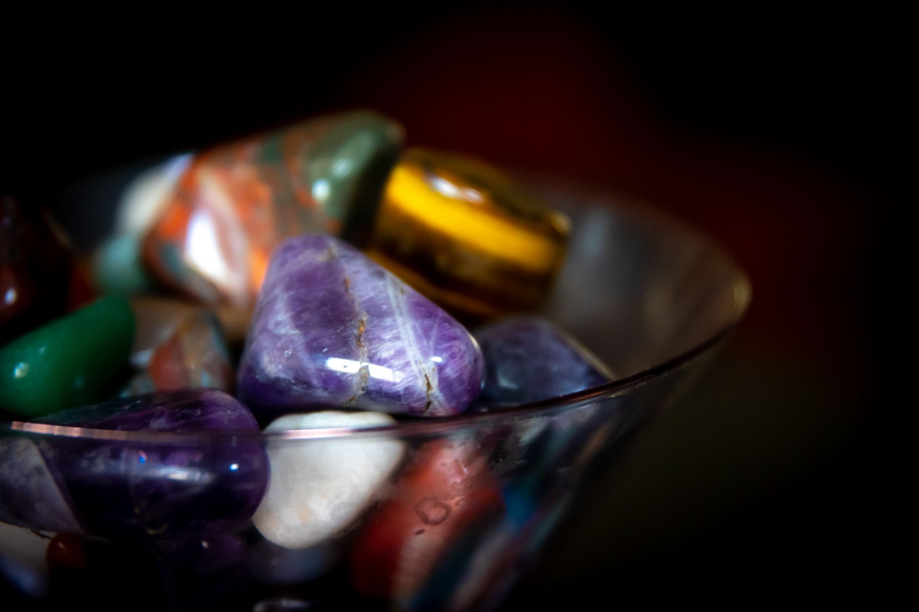 Close-up of vibrant polished gemstones displayed in a glass bowl indoors.