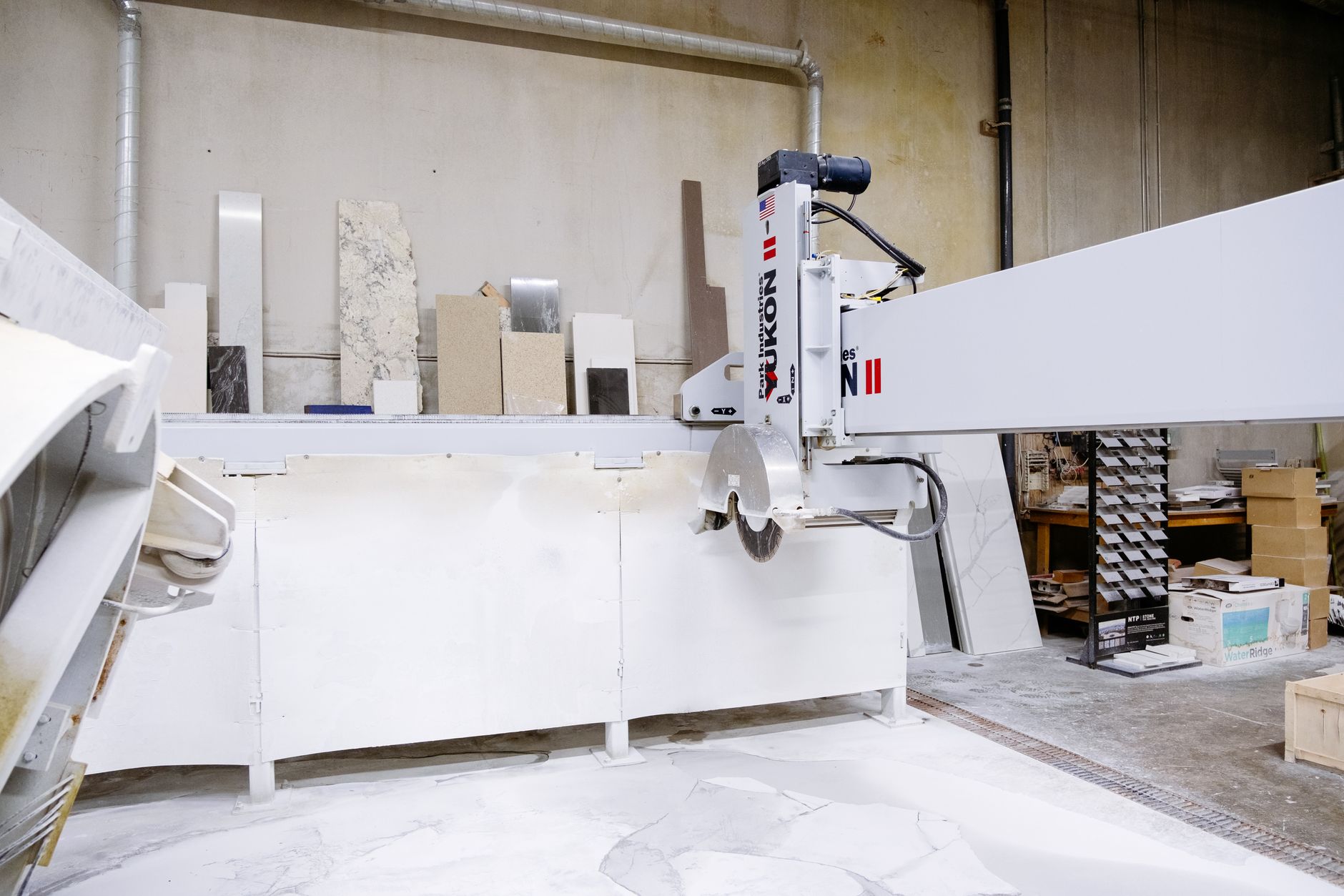 hands in gloves feeding a stone slab through a wet tile saw