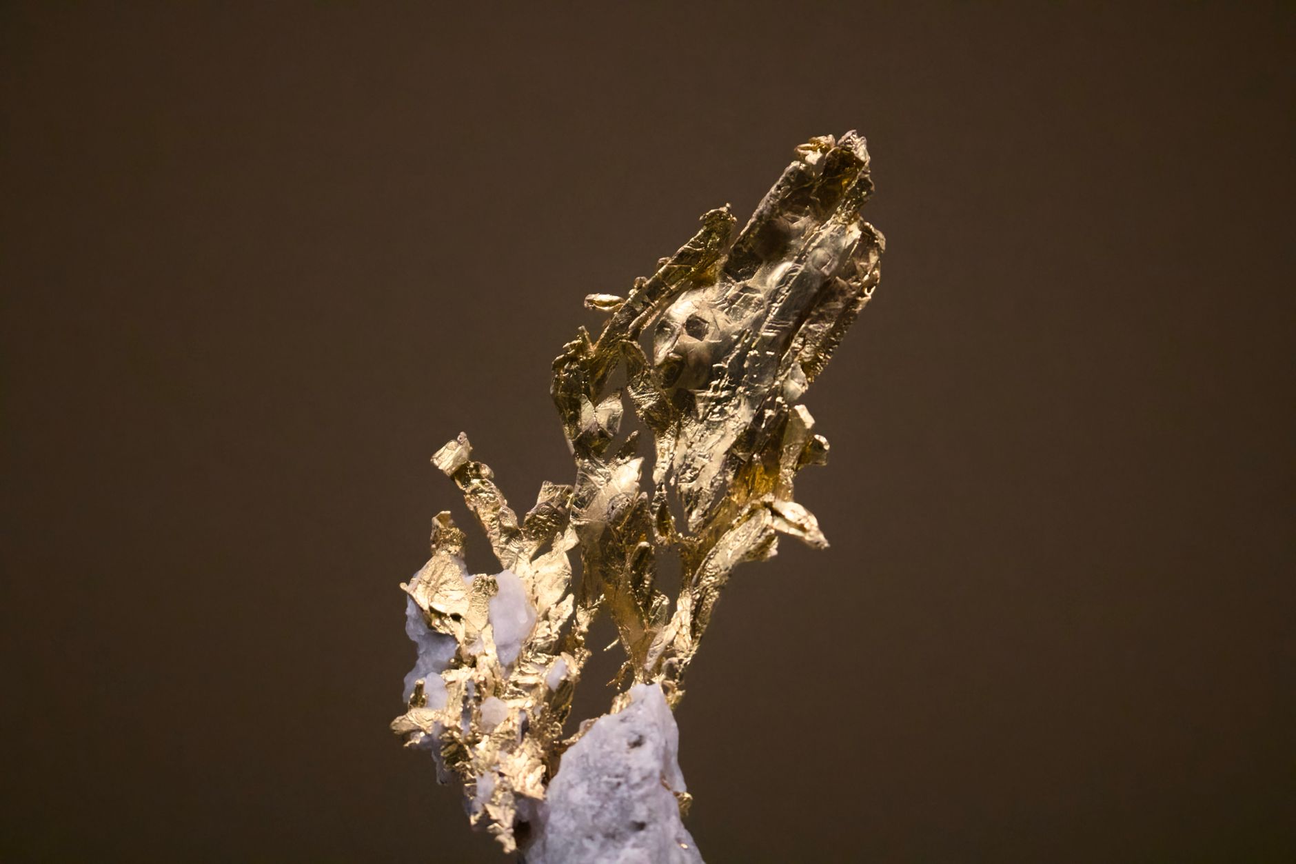 a hand pressing a steel pin into a small gold-colored nugget on a rock surface