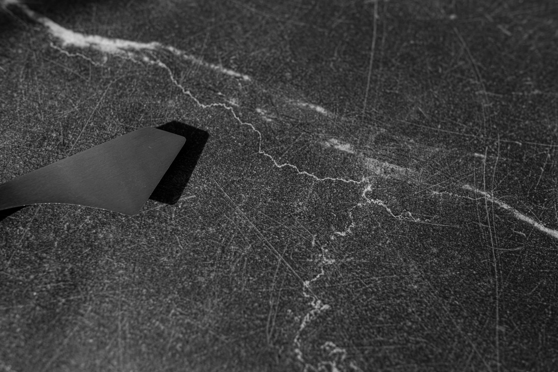 Person testing mineral hardness by scratching a specimen with a steel knife next to glass
