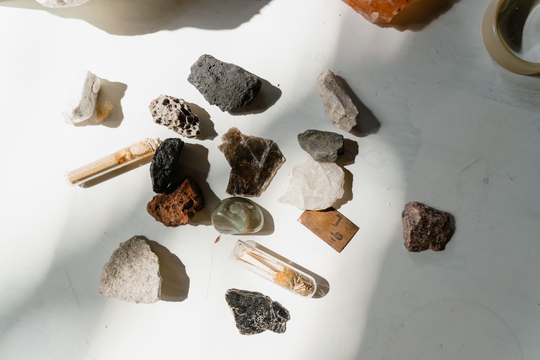 A lapidary workbench with mineral specimens, a hand lens, and hardness testing tools