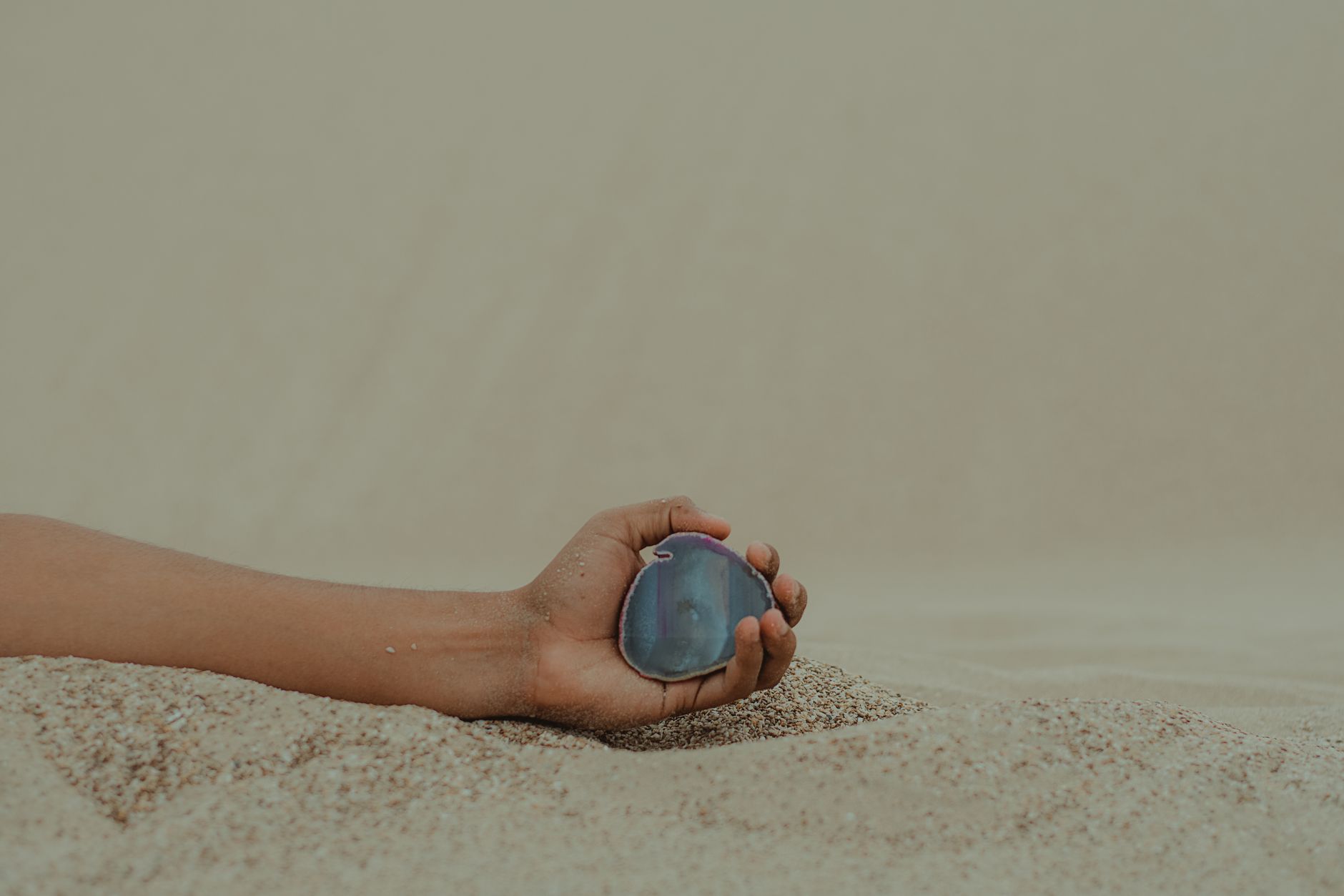 a small black shark tooth held between fingers on a sandy beach