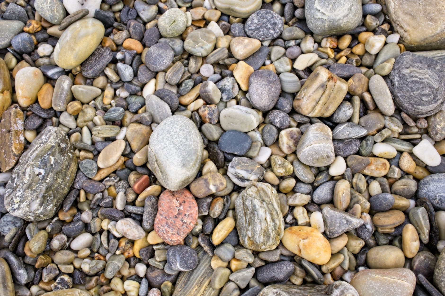 rockhound crouching on a river gravel bar with a bucket and rock hammer