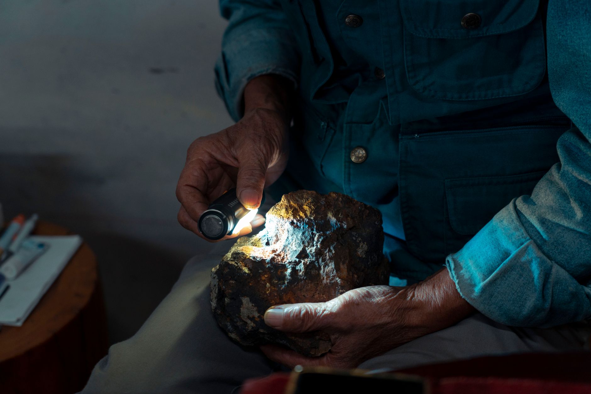 A field collector holds a hand lens over a fossil shell impression in a limestone rock
